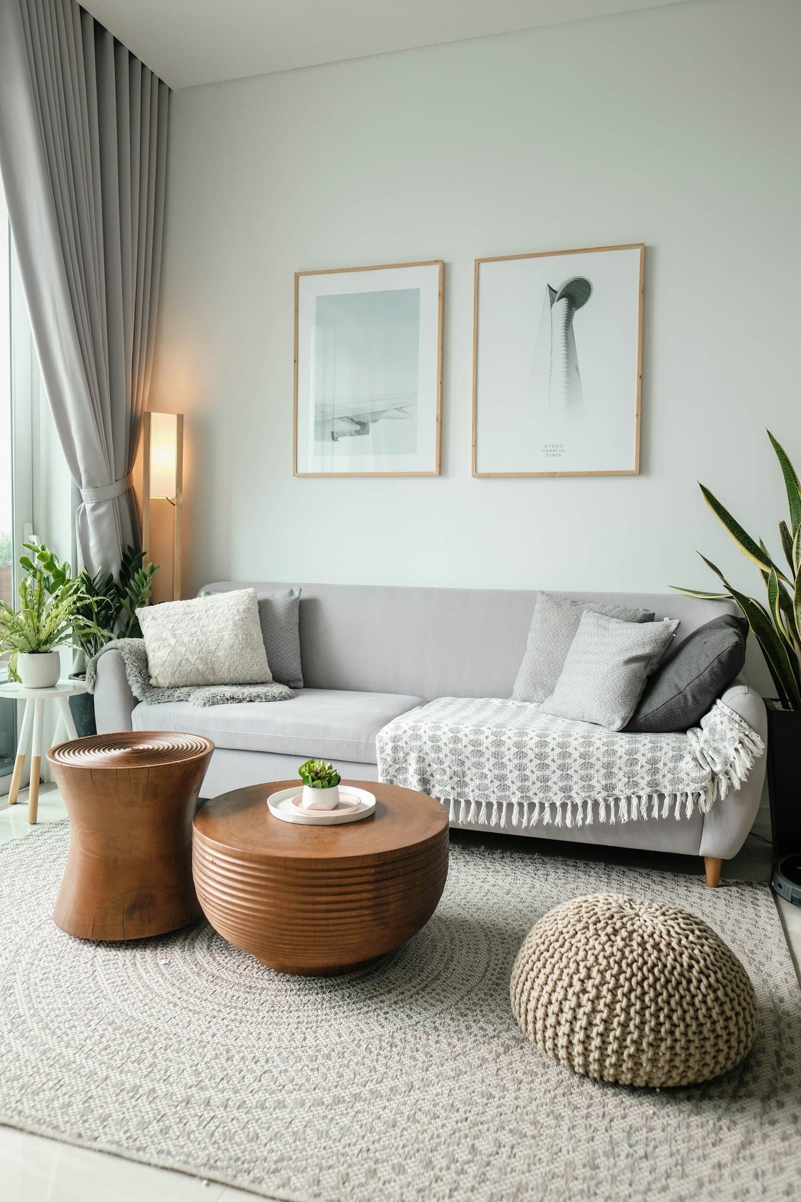 A bright rental living room with a neutral sofa, layered pillows and framed prints leaned on the wall.
