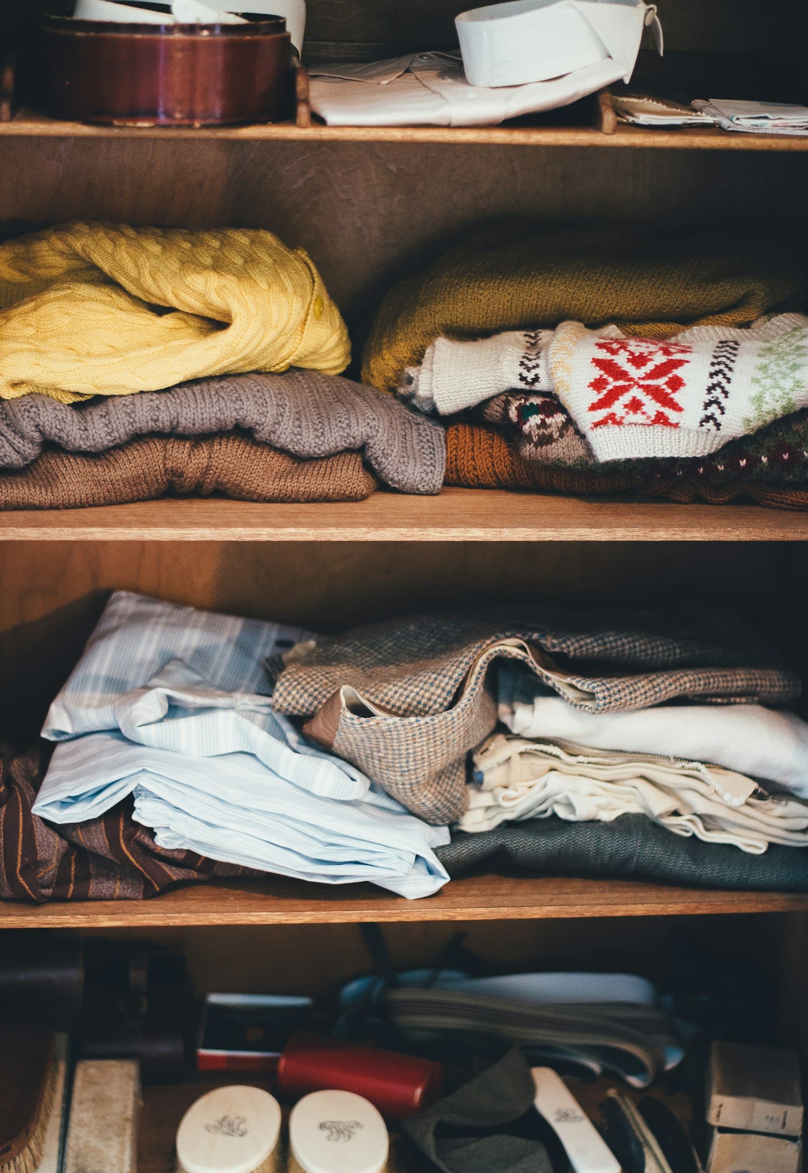 Neatly folded sweaters and linens organized on open wardrobe shelving.