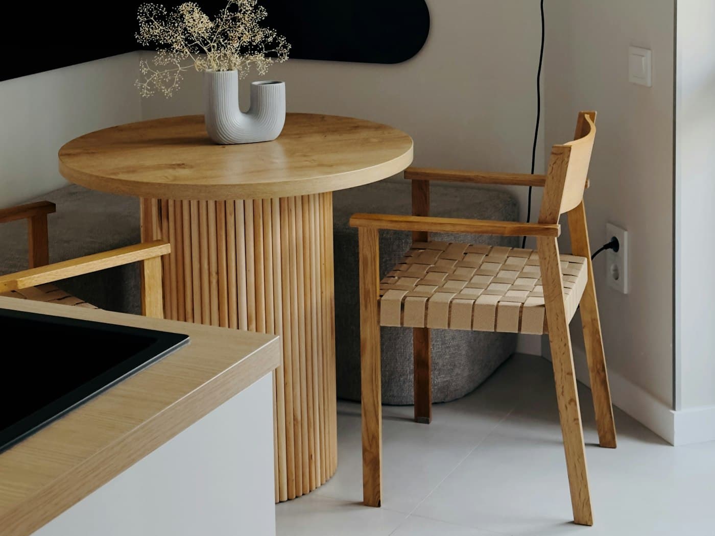 A small round wood dining table with a woven-seat chair positioned just off a kitchen counter with an integrated sink, adding seating without blocking movement.