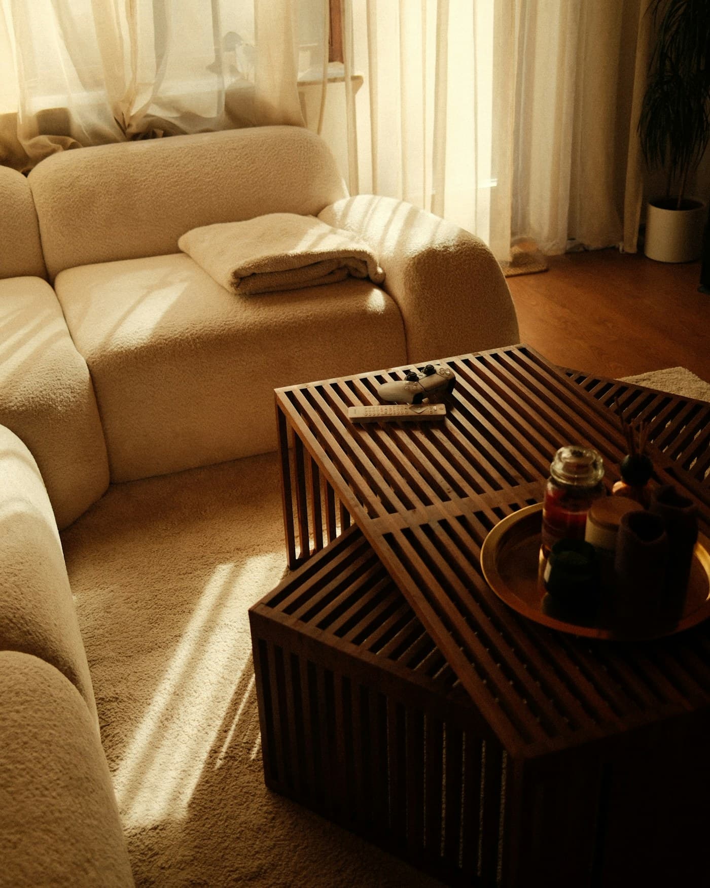 A warm, sunlit living room with a soft boucle sofa and a slatted wood coffee table