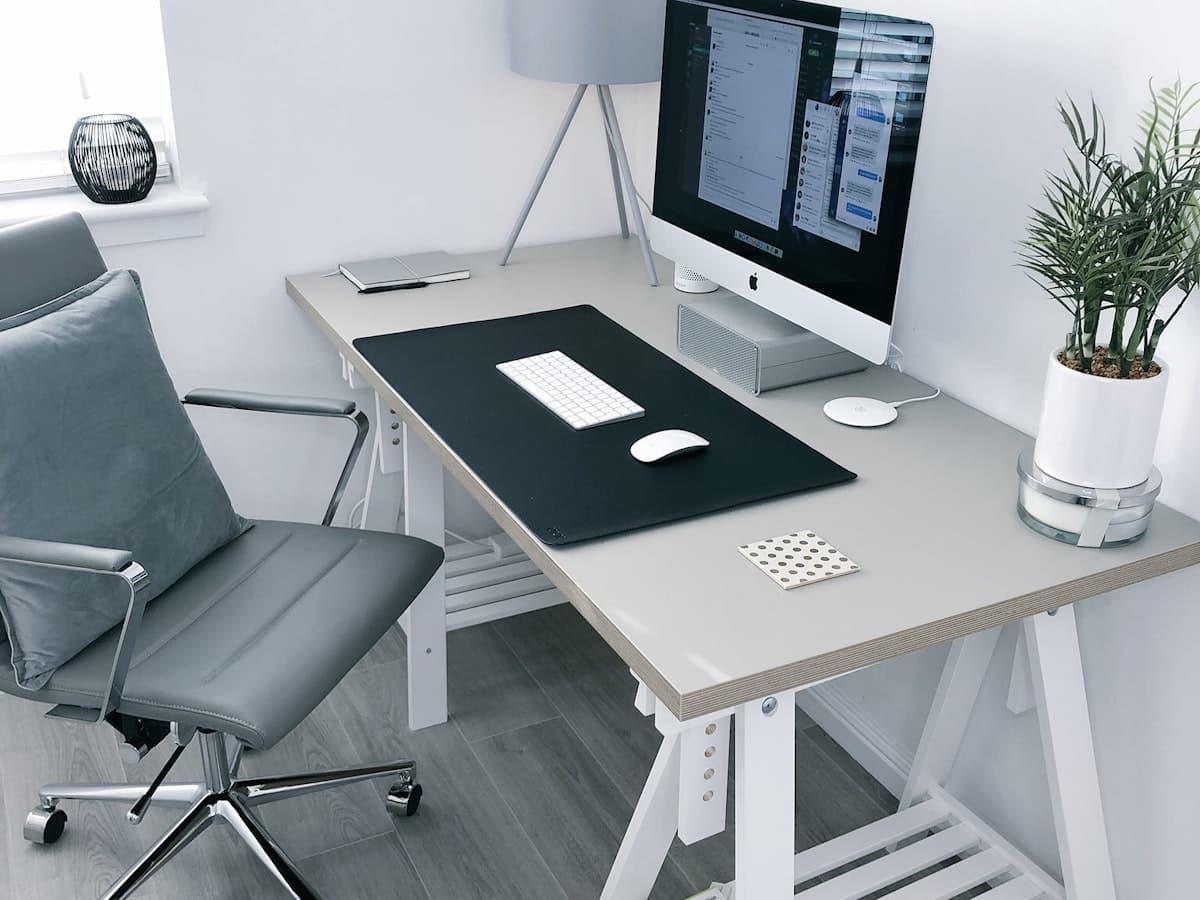 A calm, functional home office corner with a desk, chair, monitor and a small plant.